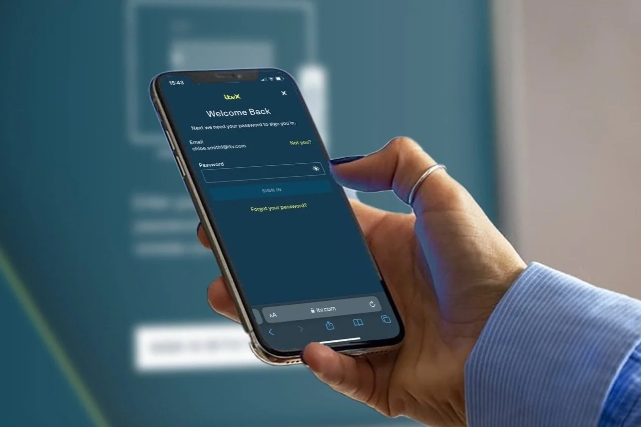 Close up of hand holding mobile phone logging in to the ITVX app with the app also on the tv in the background