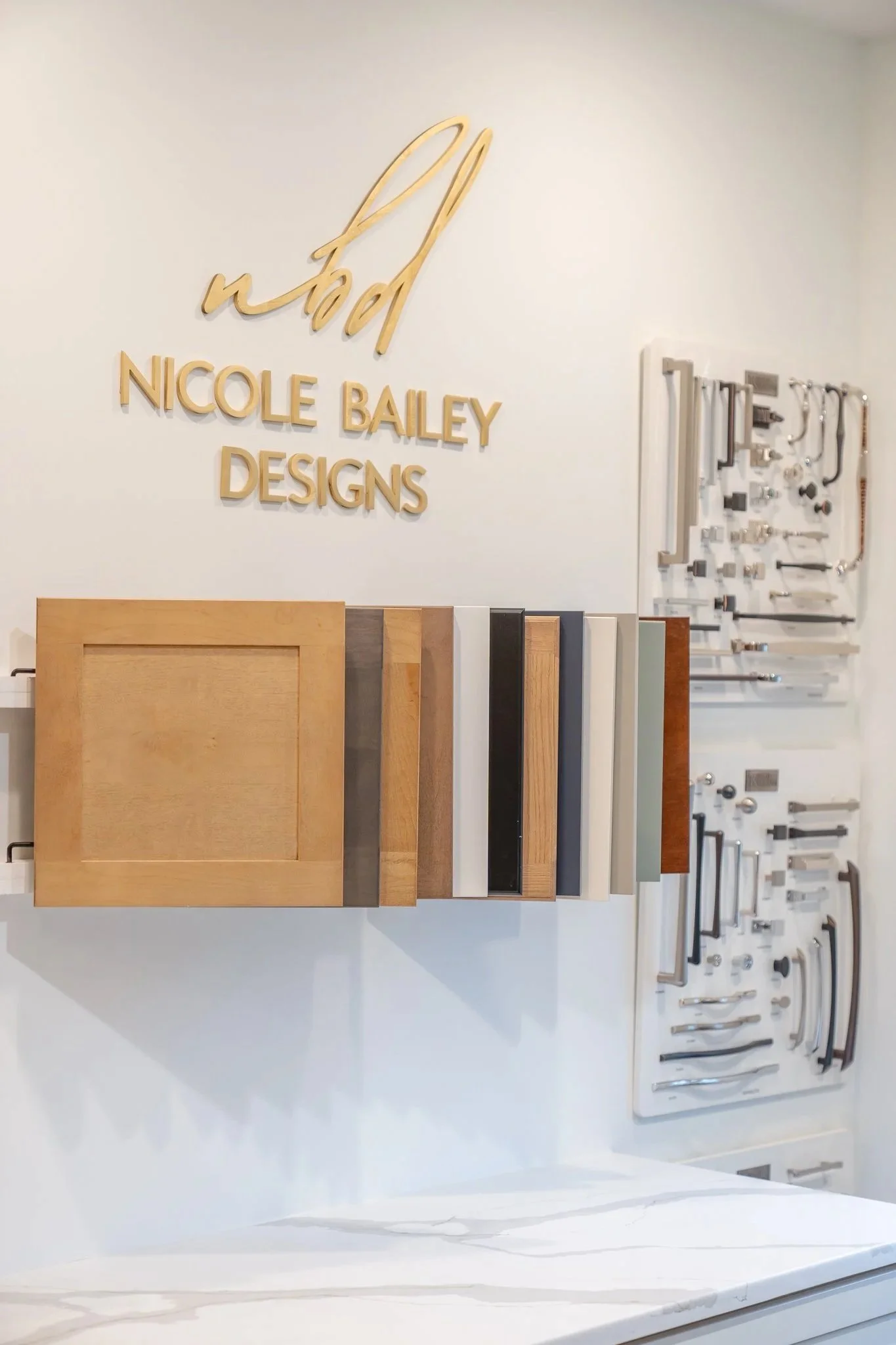 Display of wood and cabinet samples, with a sign reading 'Nicole Bailey Designs' on the wall.