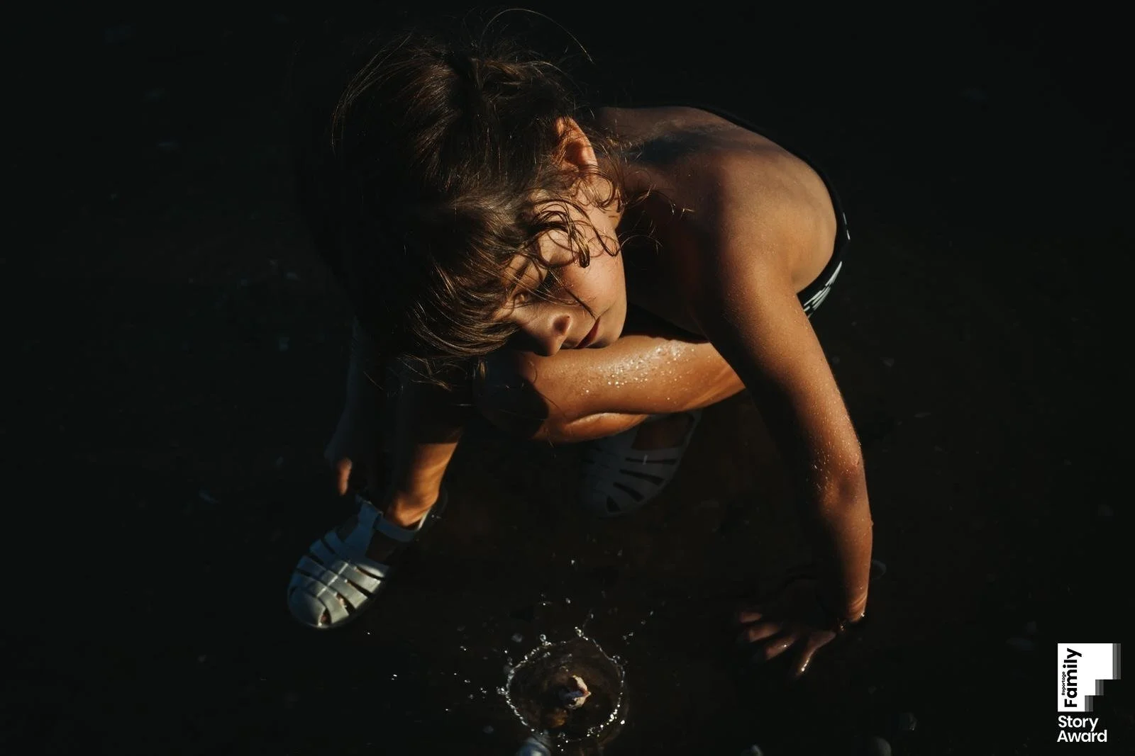 girl in dark background buttoning the show looking at a shell falling in the water