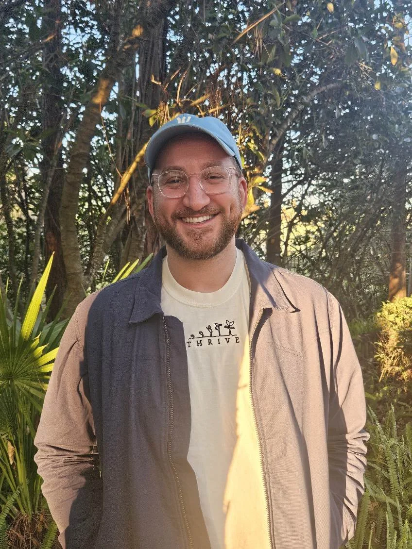 a photo of a tall white man standing outside with trees in the background