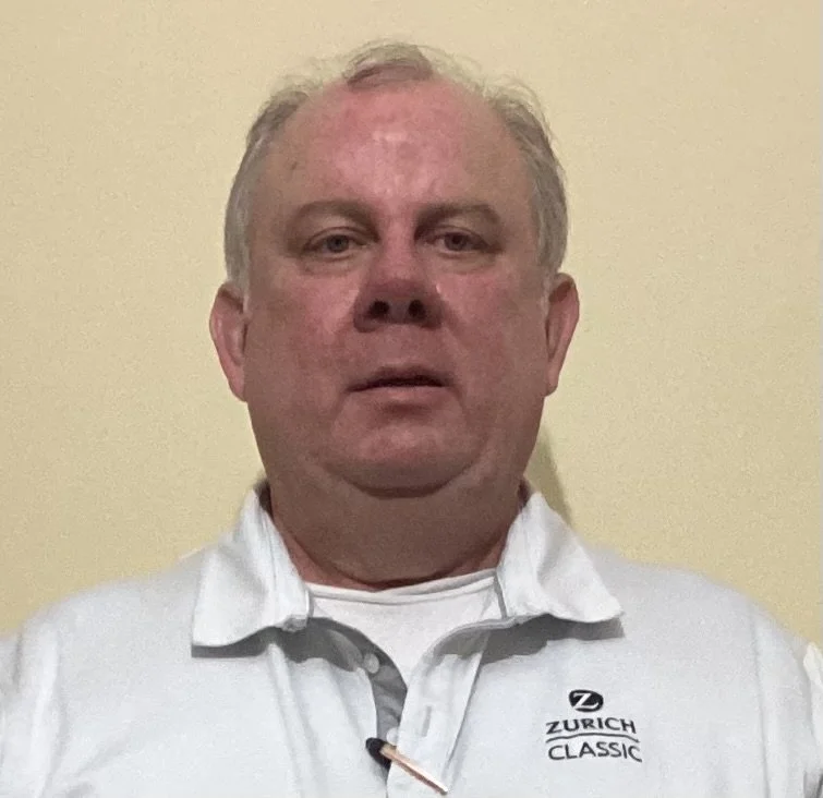 A middle-aged man with short gray hair, wearing a white polo shirt with the Zurich Classic logo, standing against a beige wall.
