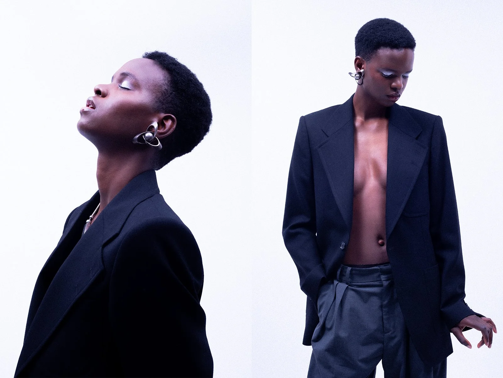 Two stylish black women dressed in dark suits, one with eyes closed and head tilted back, the other with cropped hair looking down, standing against a plain white background.
