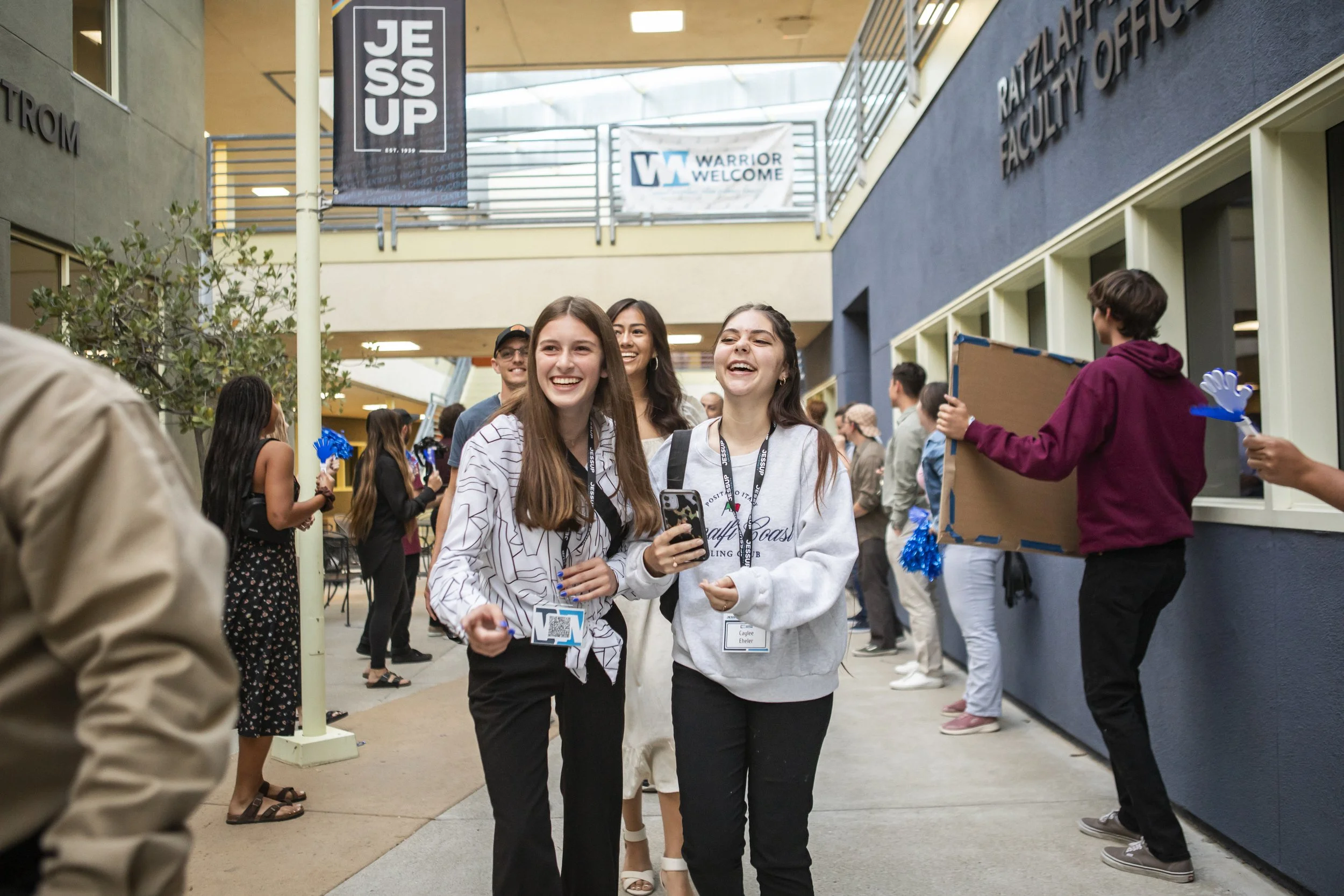 Group of young people walking and laughing in a lively indoor campus building, with banners hanging above.