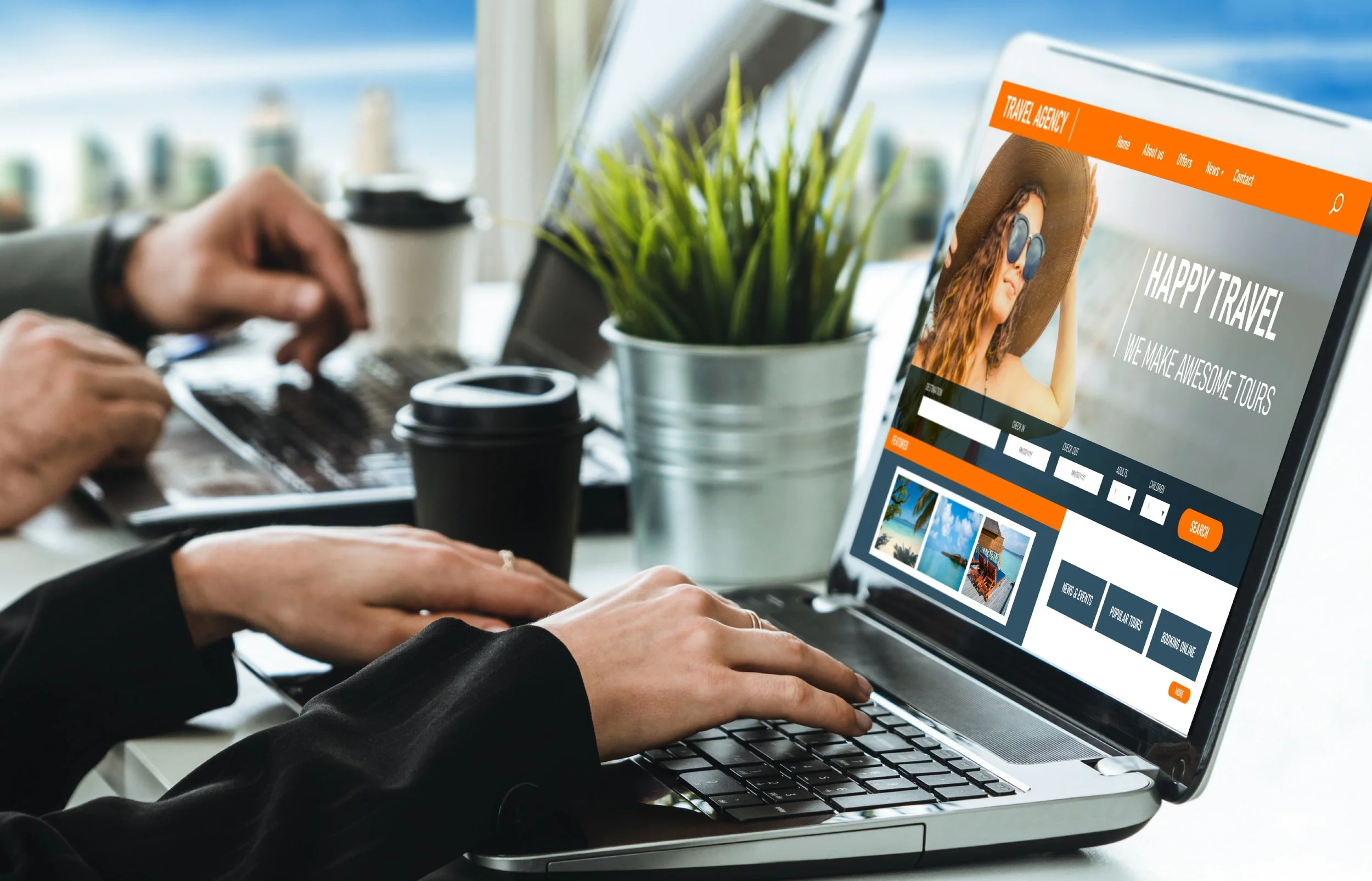 People working on laptops at a desk, with a travel website open on one screen showing vacation photos and options for tours.