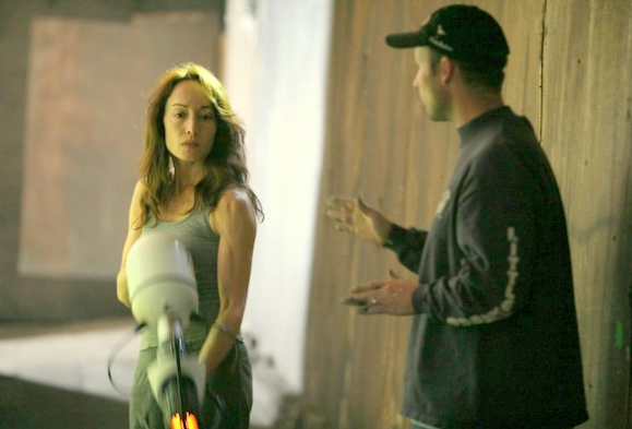 A woman and a man are having a conversation in an alleyway or narrow street. The woman looks slightly upset or contemplative, while the man is gesturing with his hands.