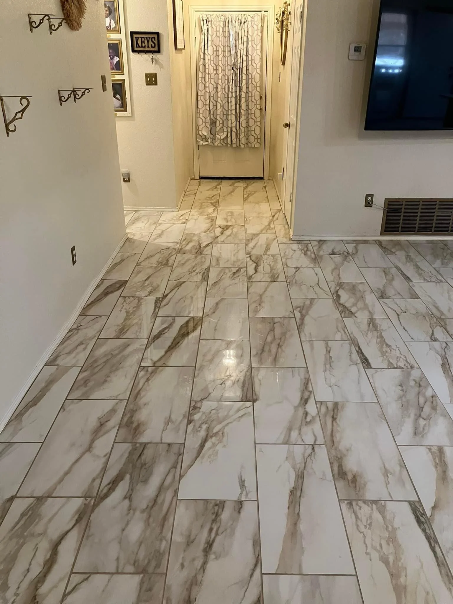 A hallway with marble tile flooring, a door with a curtain, and various wall decorations including a sign labeled 'KEYS' and framed photos.