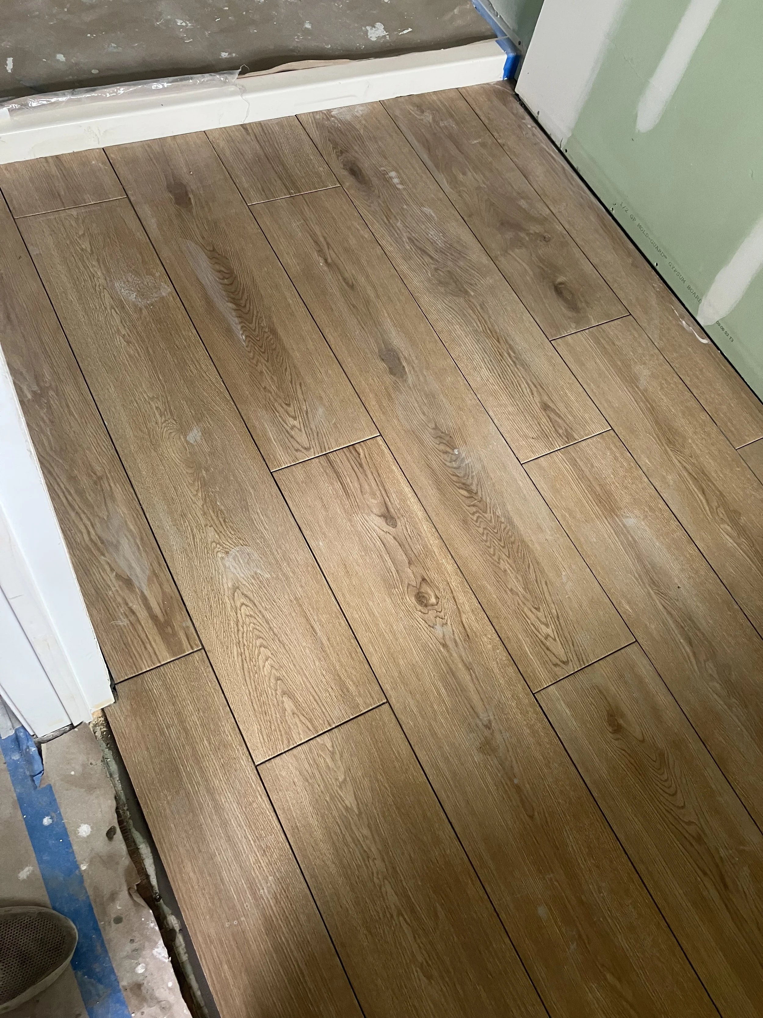 A close-up view of wooden flooring being installed in a room, with some construction materials and tools visible at the edges.