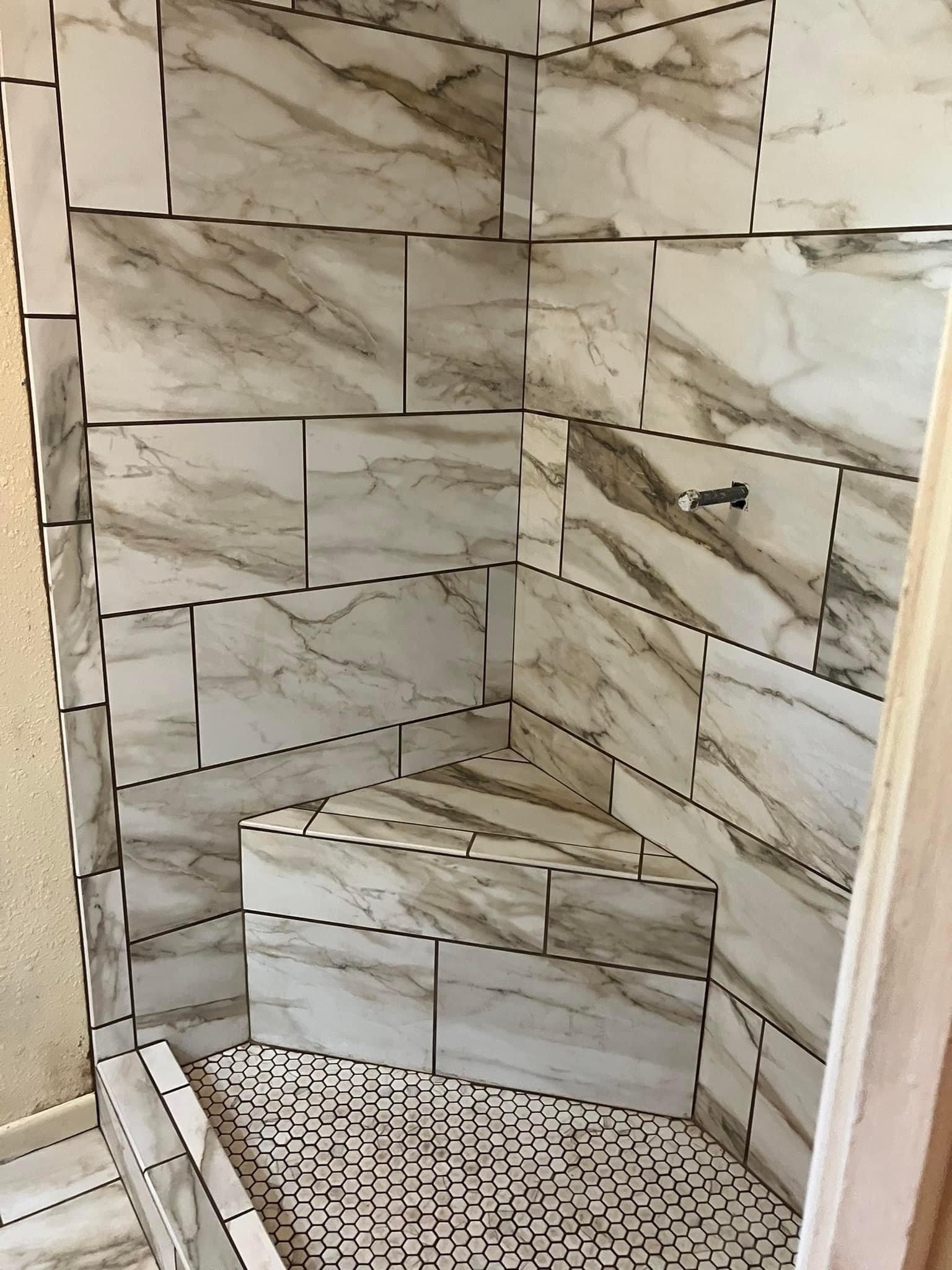 Marble tile shower with marble bench and small hexagonal floor tiles.