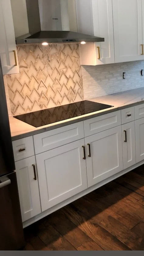 Modern kitchen with white cabinets, a black induction cooktop, a stainless steel range hood, and a decorative backsplash with a zigzag pattern.