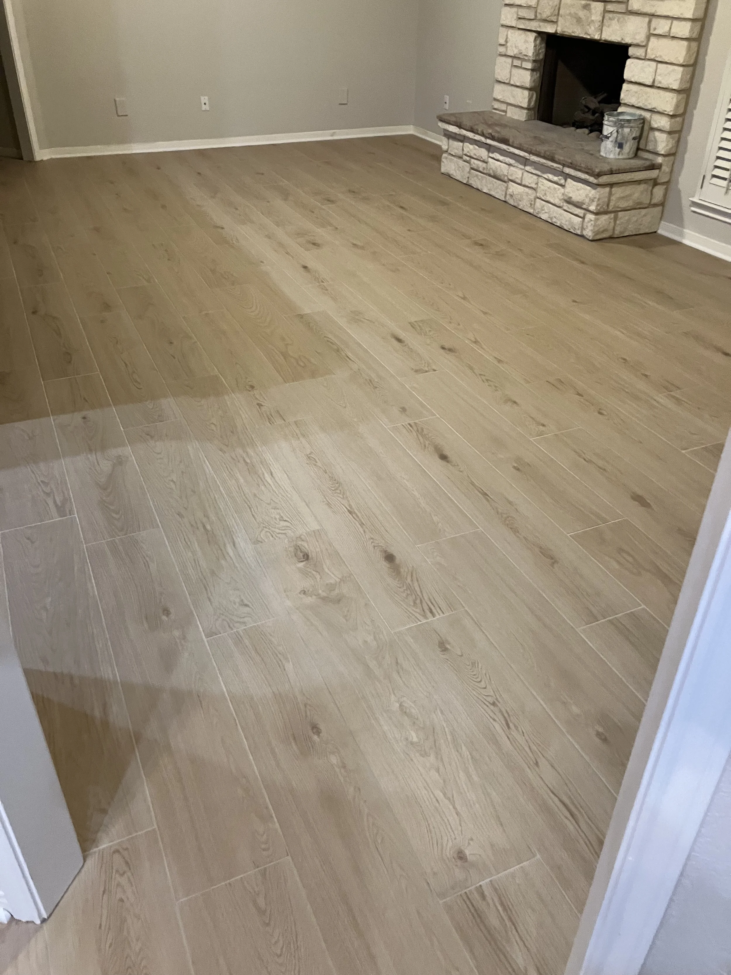 Empty living room with light-colored hardwood floors, a brick fireplace, and plain light gray walls.