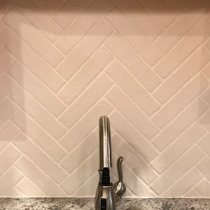 Kitchen sink with faucet against a white tile backsplash.