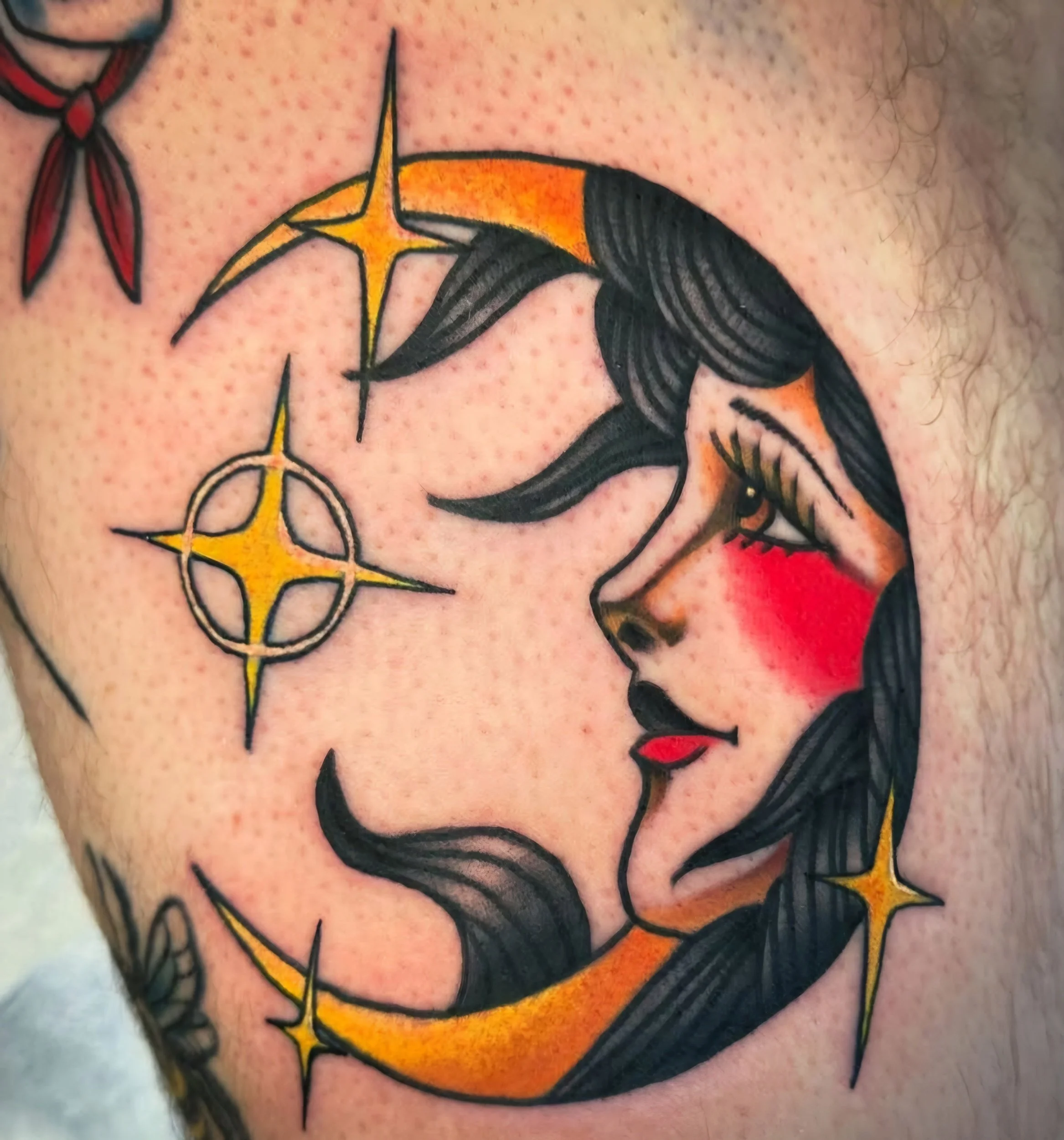Tattoo of a woman's face with dark hair and red cheeks, moon and stars, and a few smaller stars surrounding her.