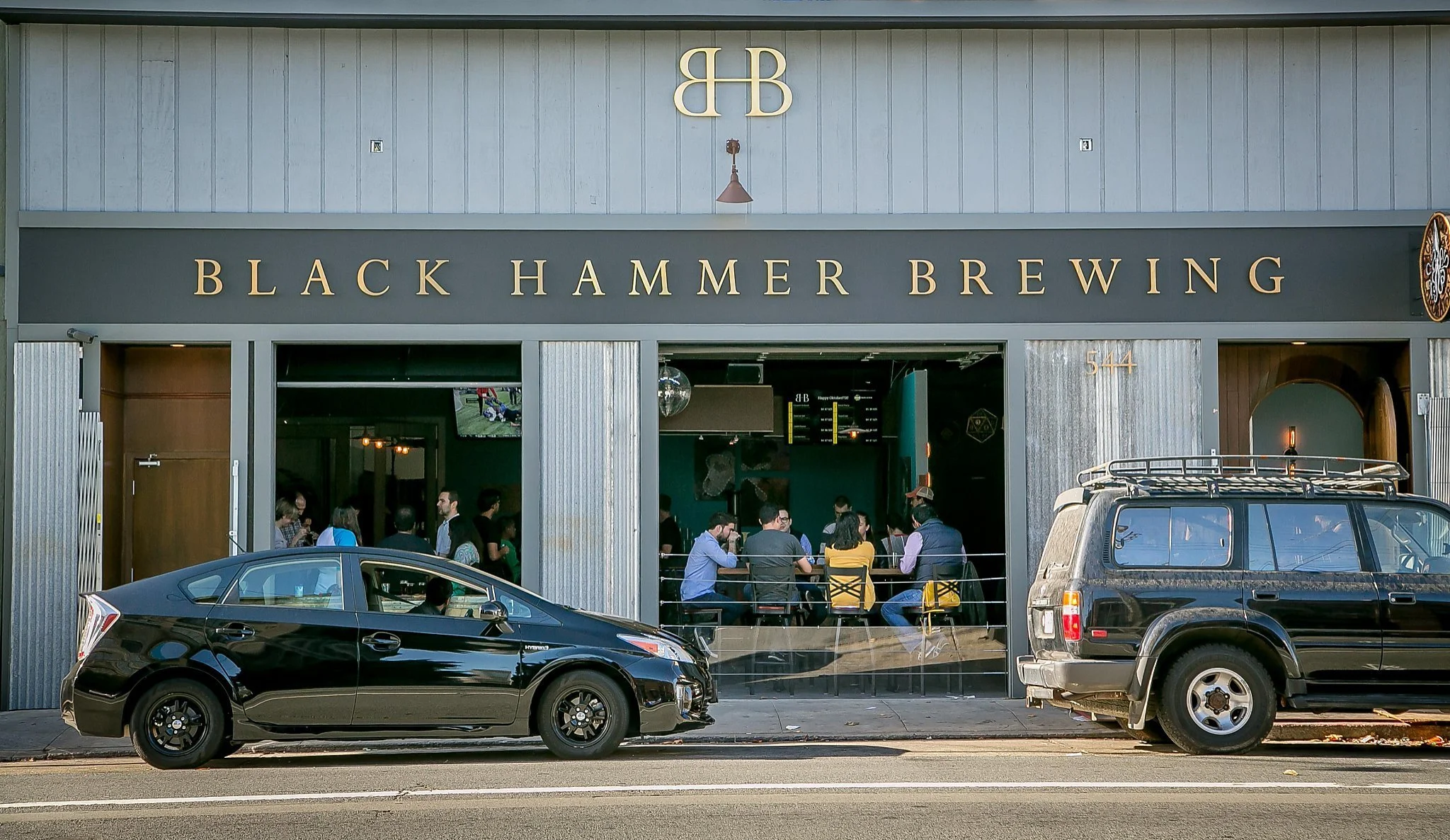 Black Hammer Brewing storefront with people inside and cars parked outside.