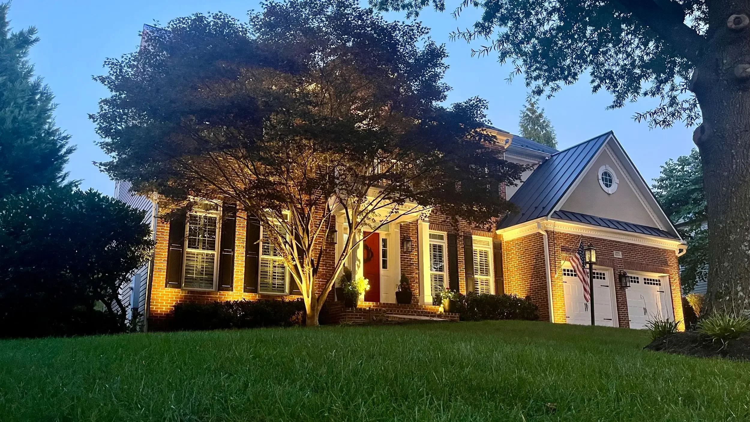The facade and surrounding trees are beautifully highlighted at dusk, creating a warm, inviting glow that showcases the home's architectural charm.