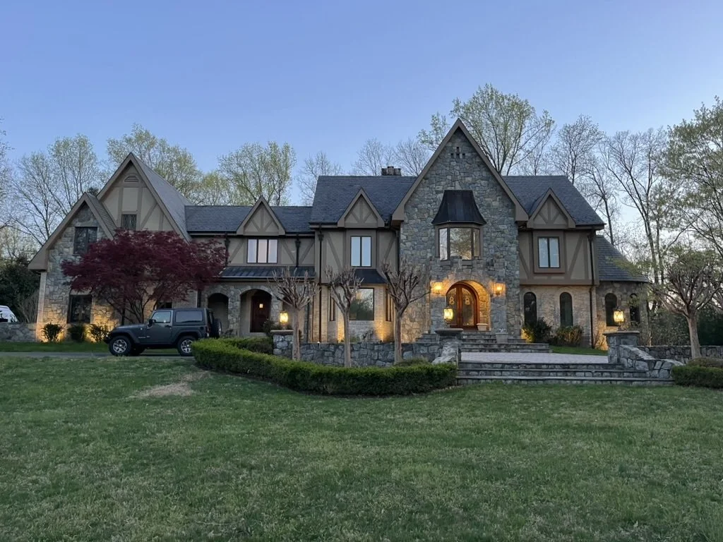 Front façade of a stone home before lighting redesign, showing limited illumination and shadowing on upper levels.