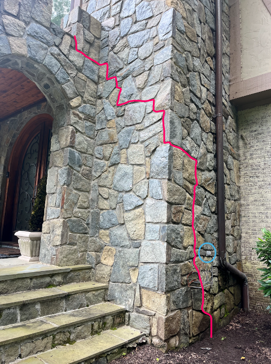 Marked-up photo of a stone home façade showing concealed wiring routed through mortar joints to power portico roof lighting fixtures.