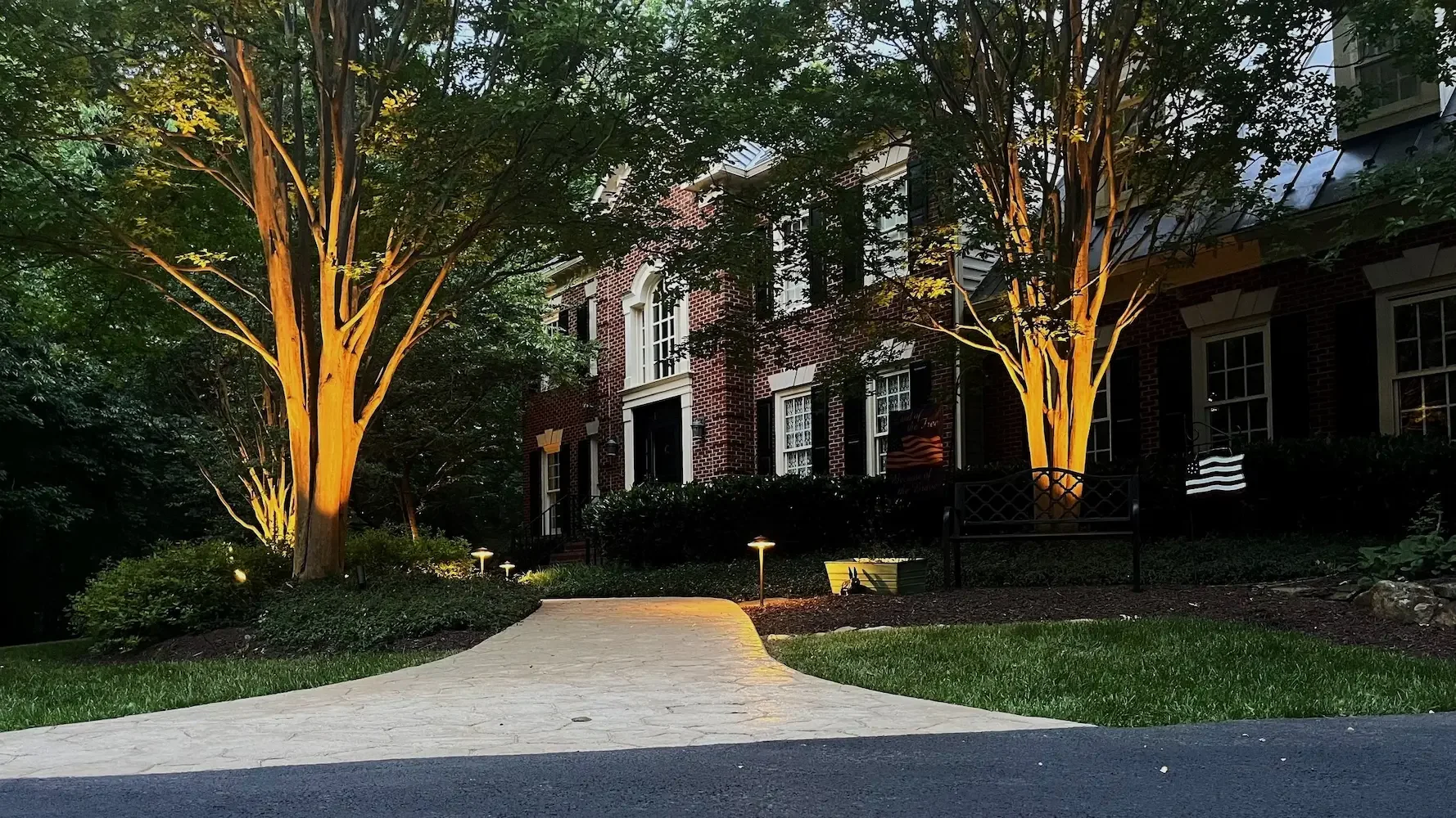 Nighttime view of a brick residential building with illuminated trees and a paved walkway leading to the entrance