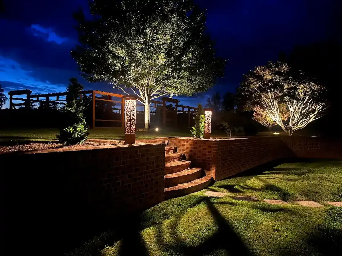 Night scene of illuminated trees, brick steps, and layered garden lighting featuring bollard lights and tree uplighting.