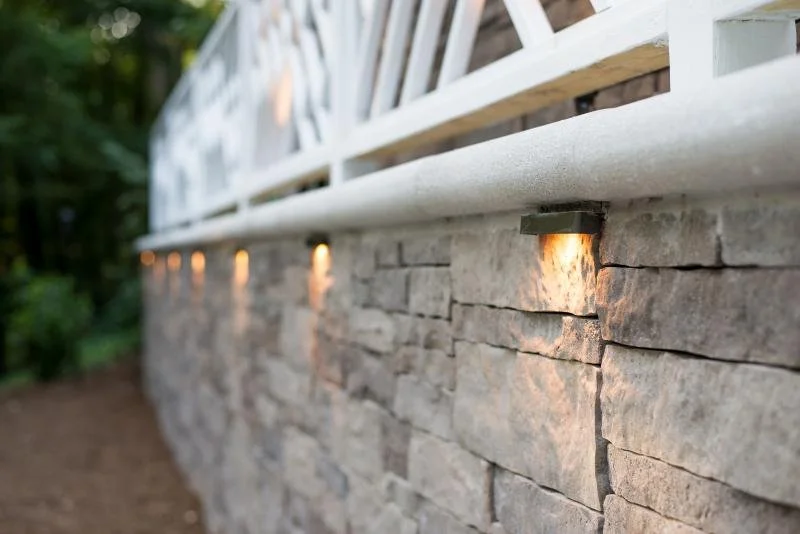 Close-up of a stone wall with embedded lighting and a white decorative railing on top.