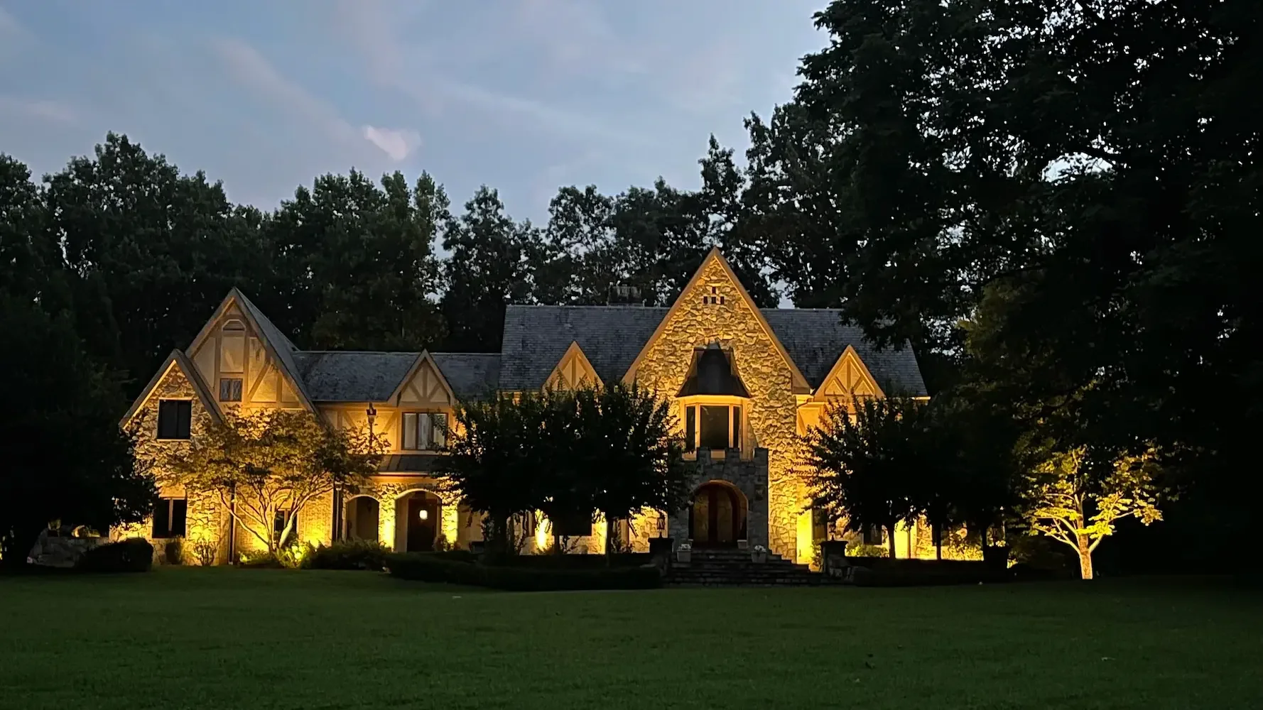 Large Great Falls house illuminated at night with trees and a well-maintained lawn in front.