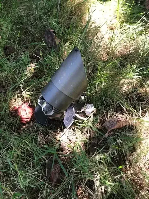 A destroyed drone lying on the grass in a wooded area.