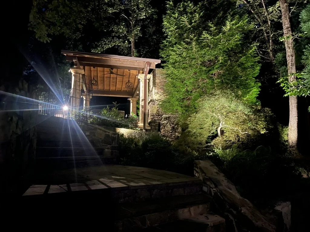 Outdoor pavilion illuminated at night with layered landscape lighting and a Tailored Lights bollard guiding the pathway on a Great Falls estate.