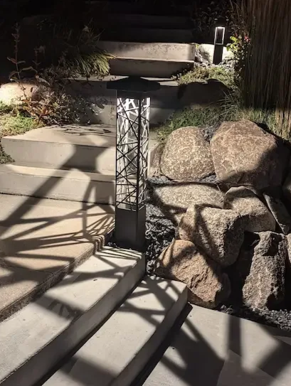 Nighttime outdoor scene with concrete stairs, a modern bollard light fixture.