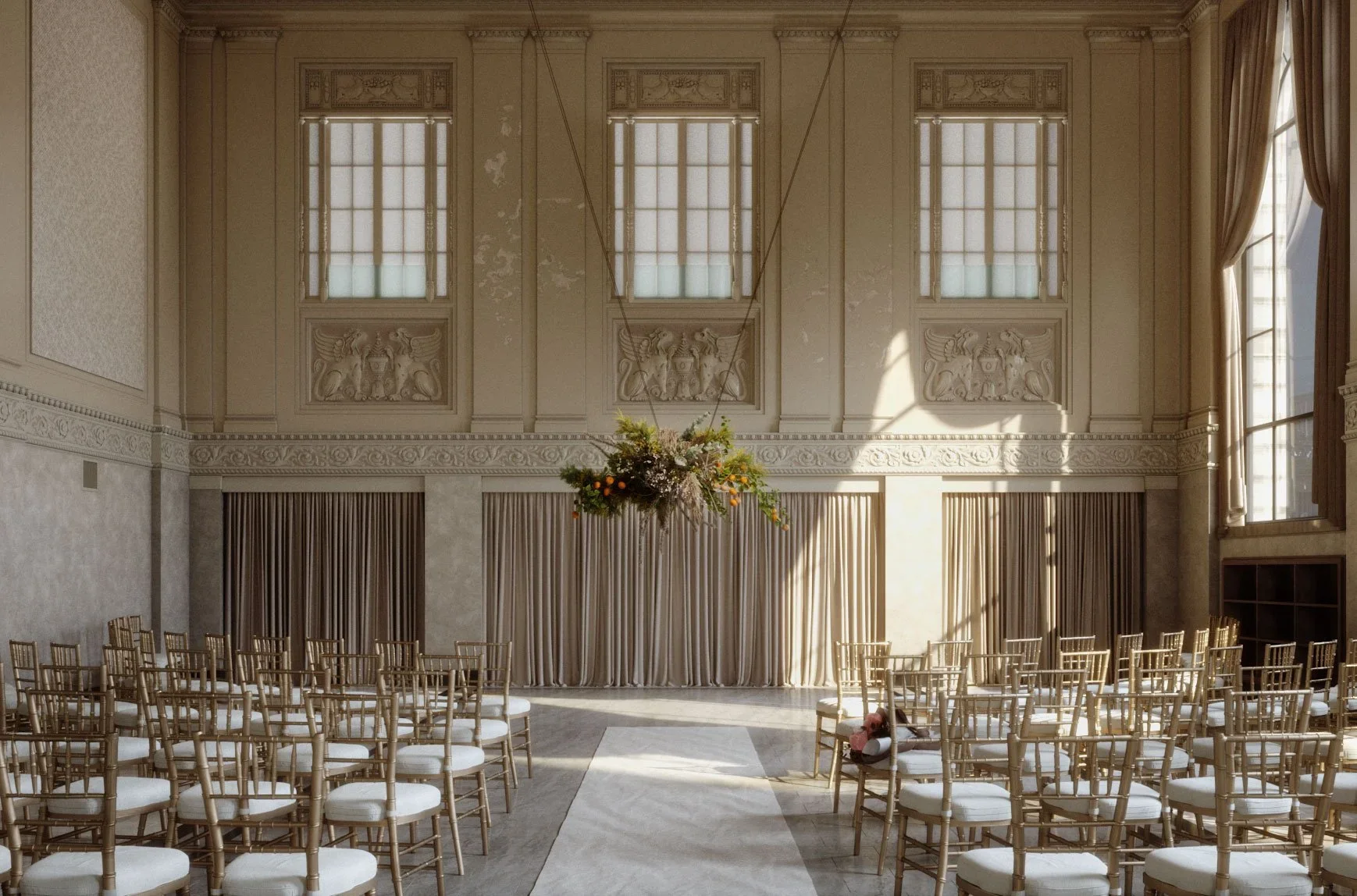 Elegant large room set up for a wedding or event with rows of white chairs with gold frames, a gray carpet aisle, high windows, ornate wall details, and a large floral hanging arrangement.