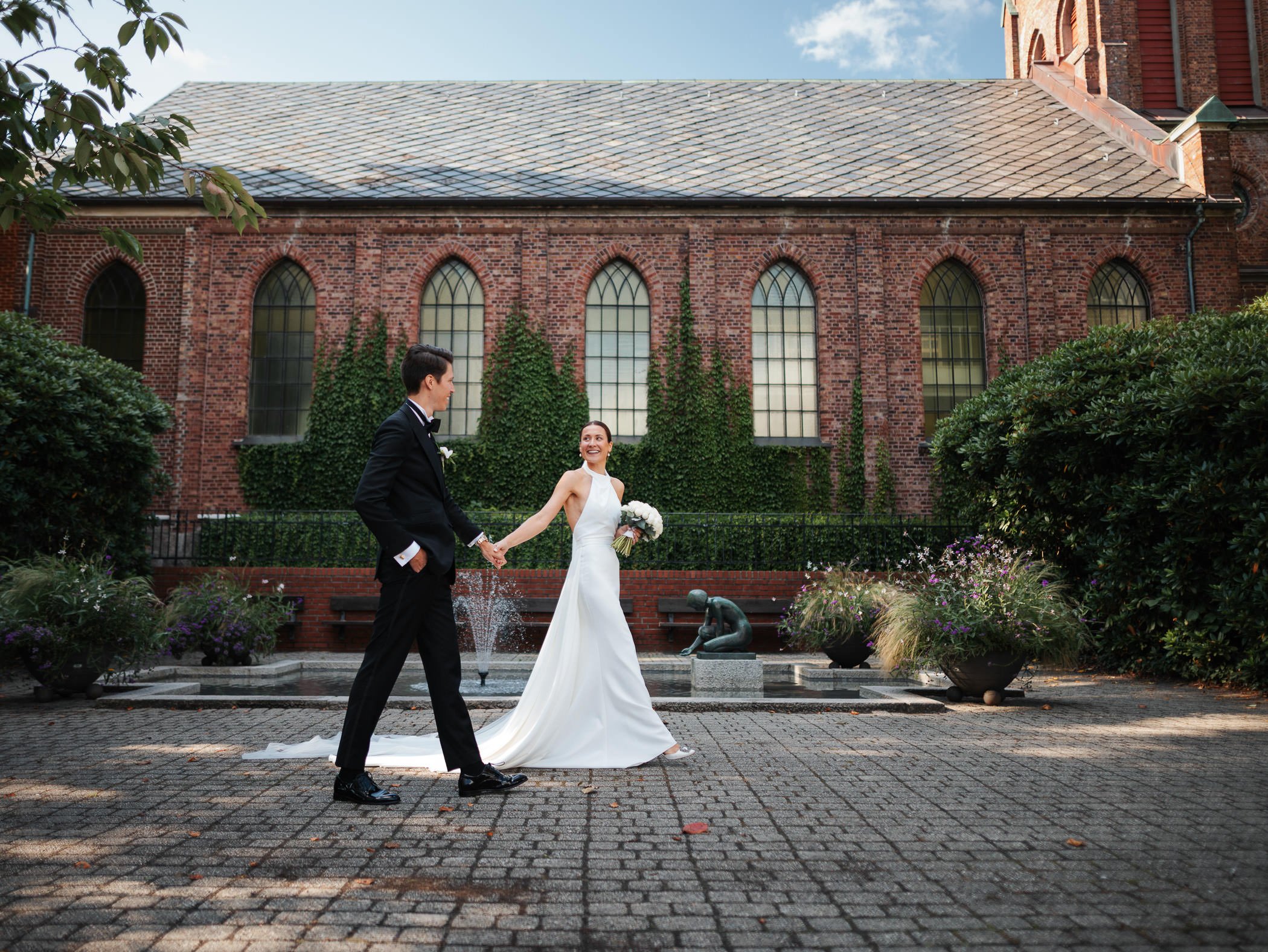 Et brudepar holder hender og går sammen og tar bryllupsbilder foran Sandnes kirke.
