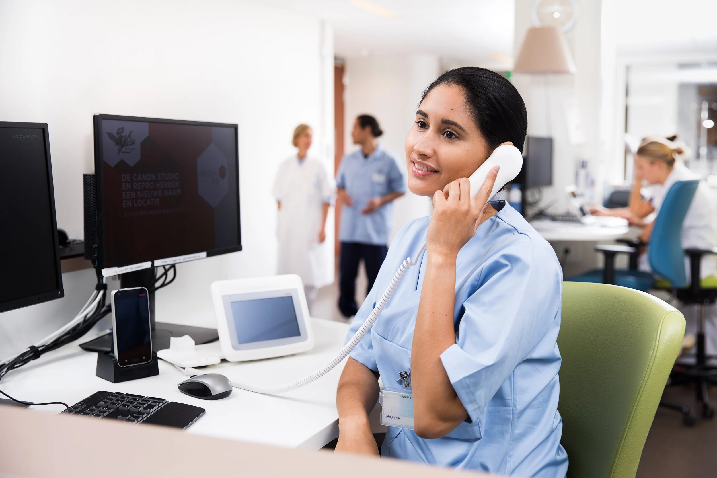 A healthcare worker talking on a telephone at her desk in a hospital or clinic setting.