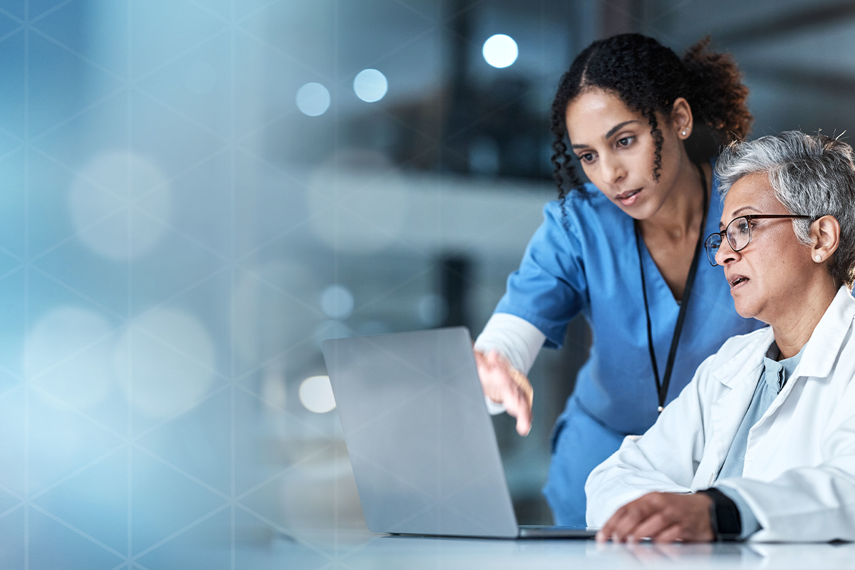 Two female healthcare professionals working together at a laptop in a modern medical facility.