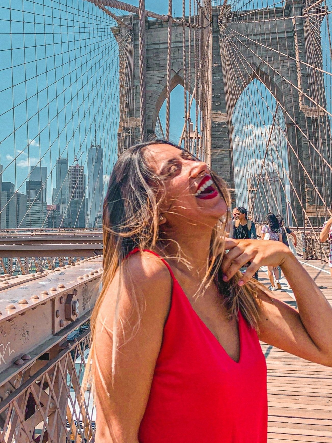 Woman in a red shirt laughing on a bridge in front of a city. This represents finding a sense of peace and enjoyment through therapy for people-pleasing