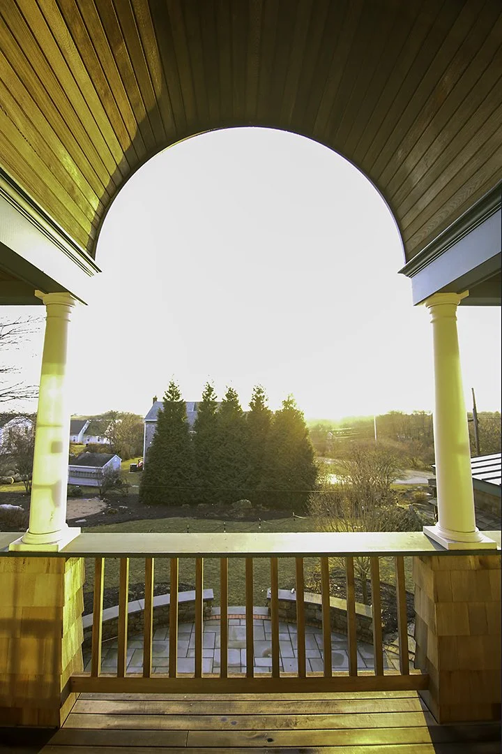 View from a balcony or porch overlooking a yard with trees, houses, and a sunset.