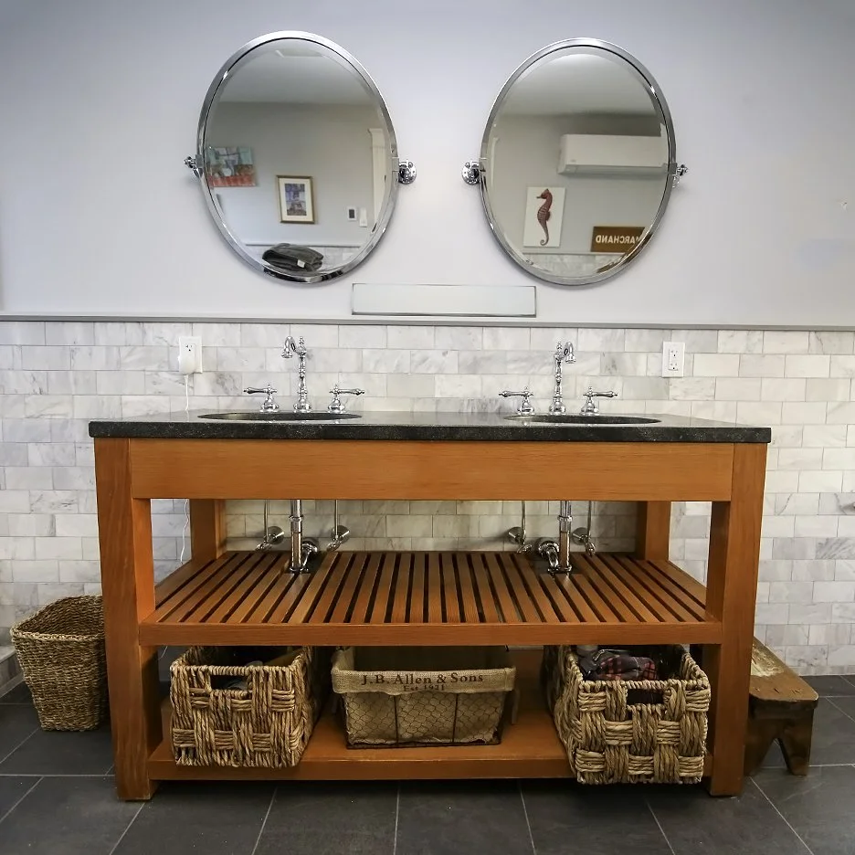 Wooden double-sink vanity with two mirrors above, white subway tile backsplash, and baskets underneath in a bathroom.
