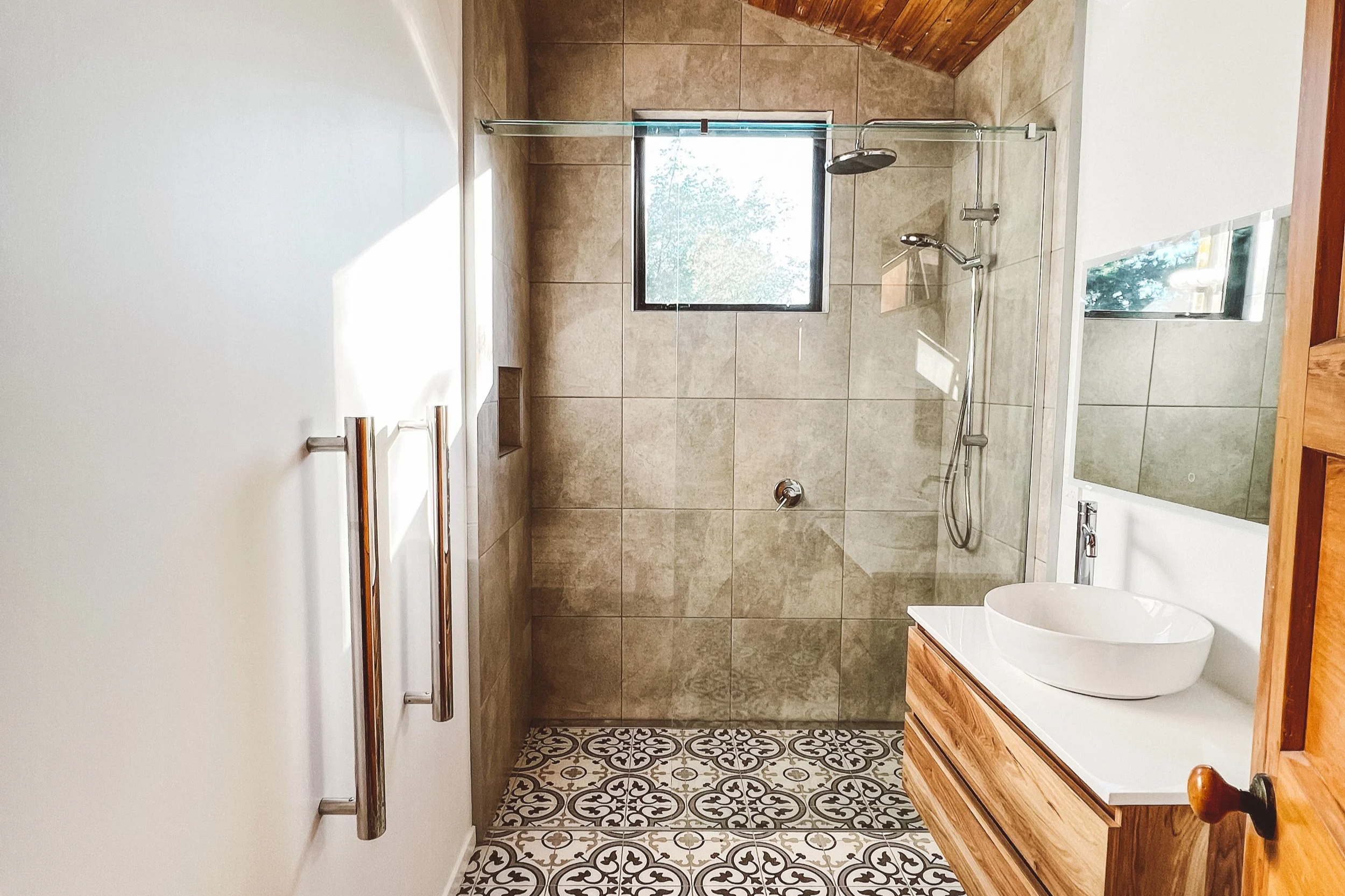 Bathroom with a walk-in shower, a small window, patterned floor tiles, wooden vanity with a vessel sink, and a mirror.