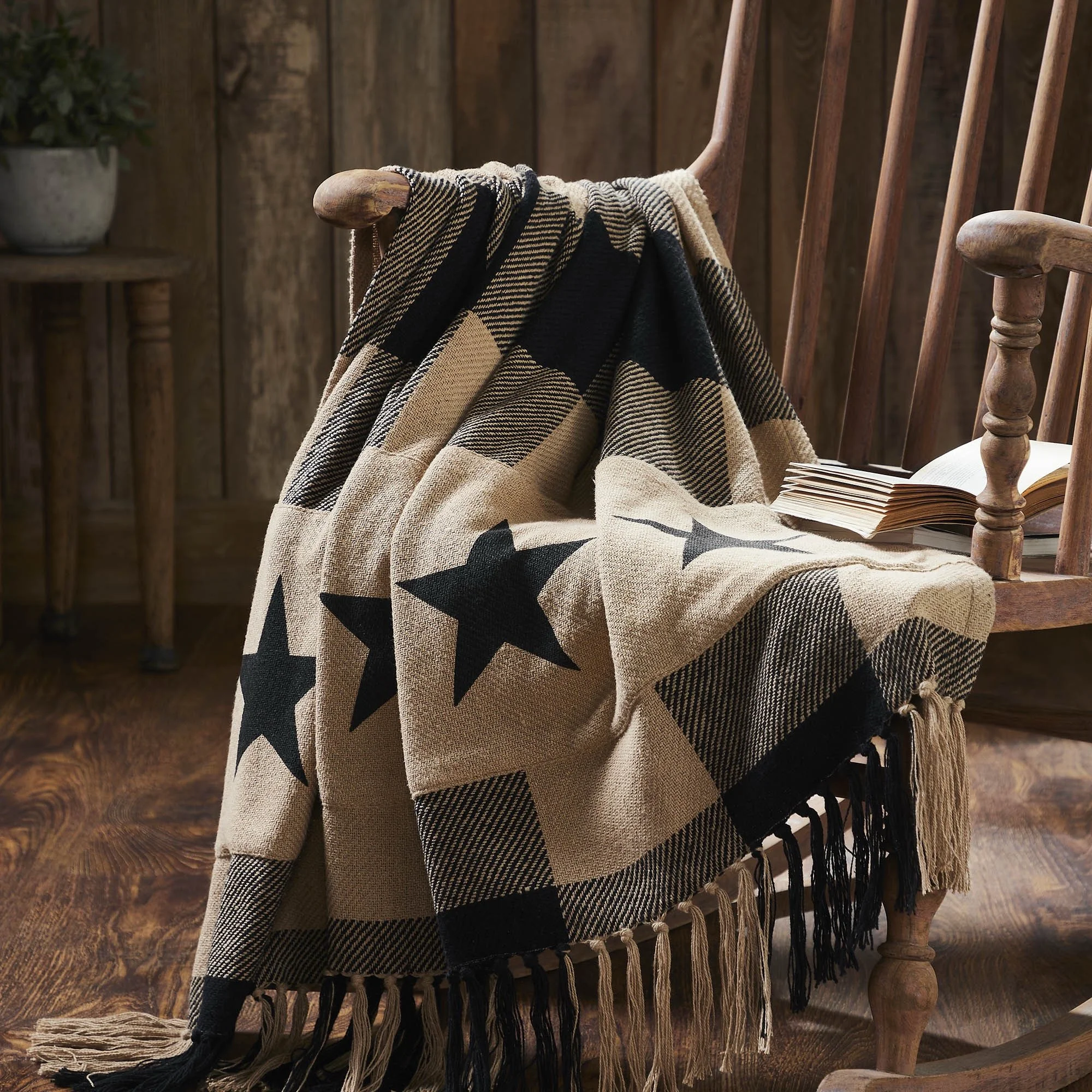A beige and black tartan blanket with star patterns draped over a wooden chair, with an open book resting on the chair's armrest, set in a rustic wooden interior.