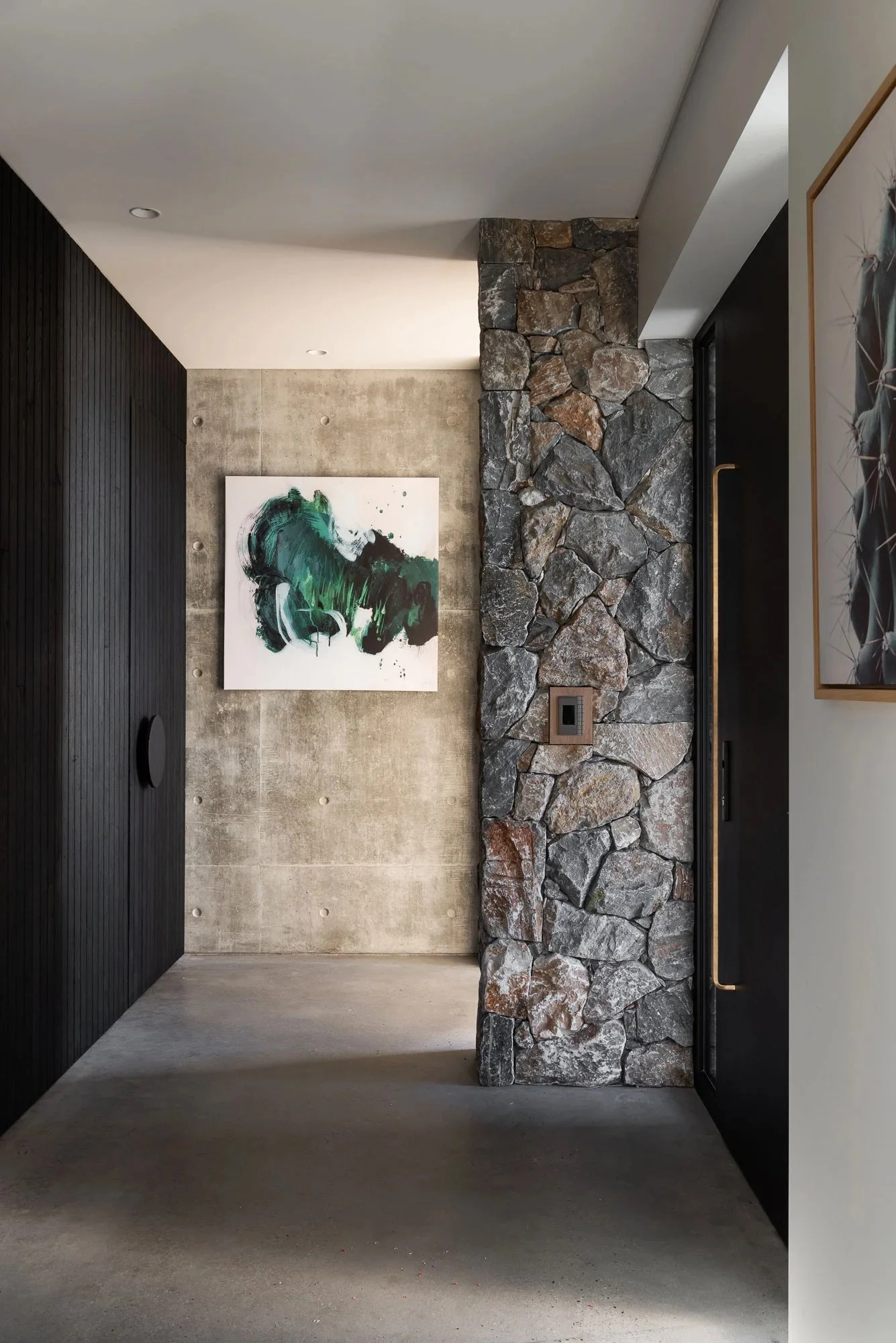 Modern house with stone and black siding exterior, paved driveway, landscaped lawn, and trees, during twilight.