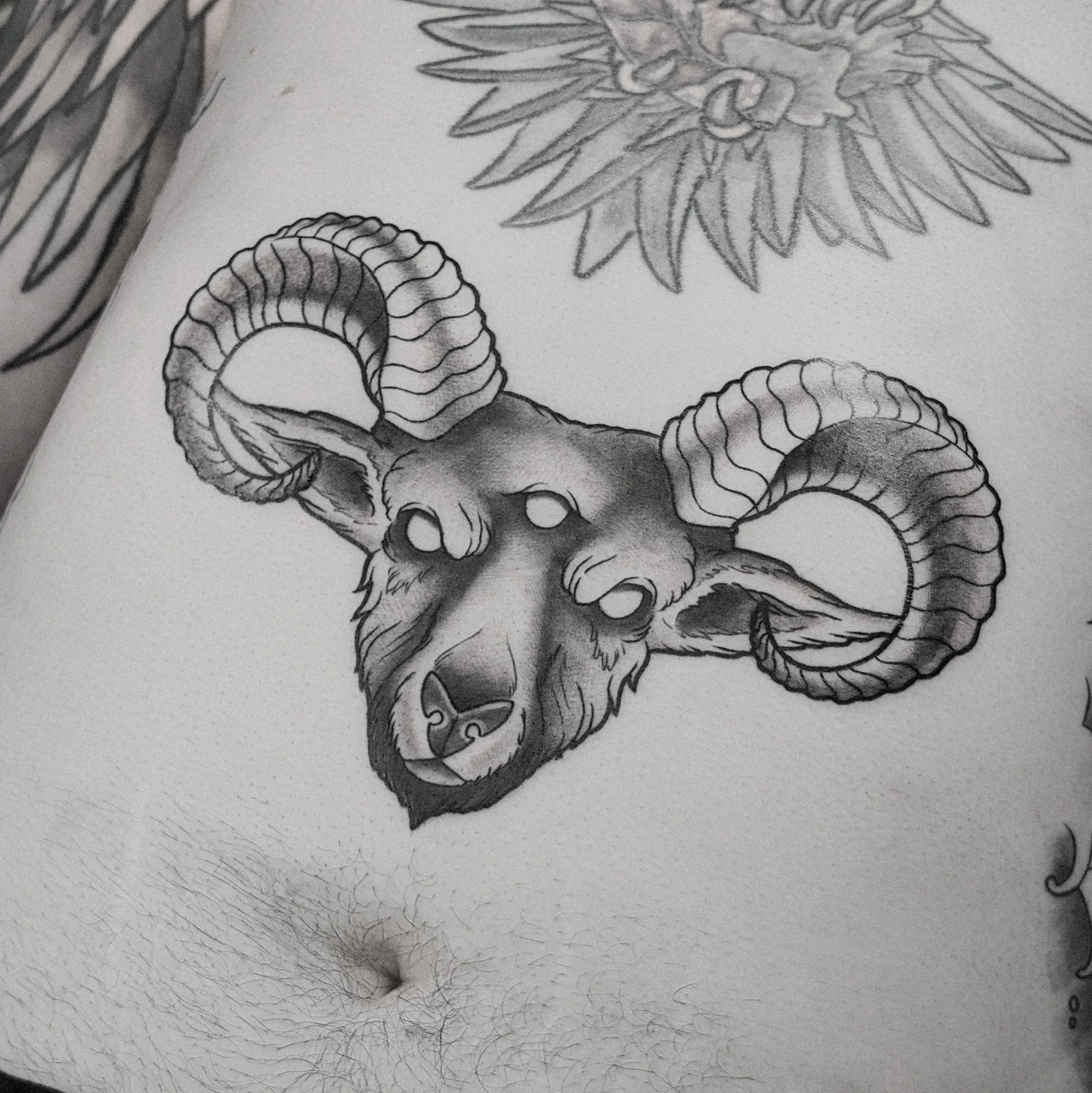 Tattoo of a ram's head with large, curled horns on person's chest.