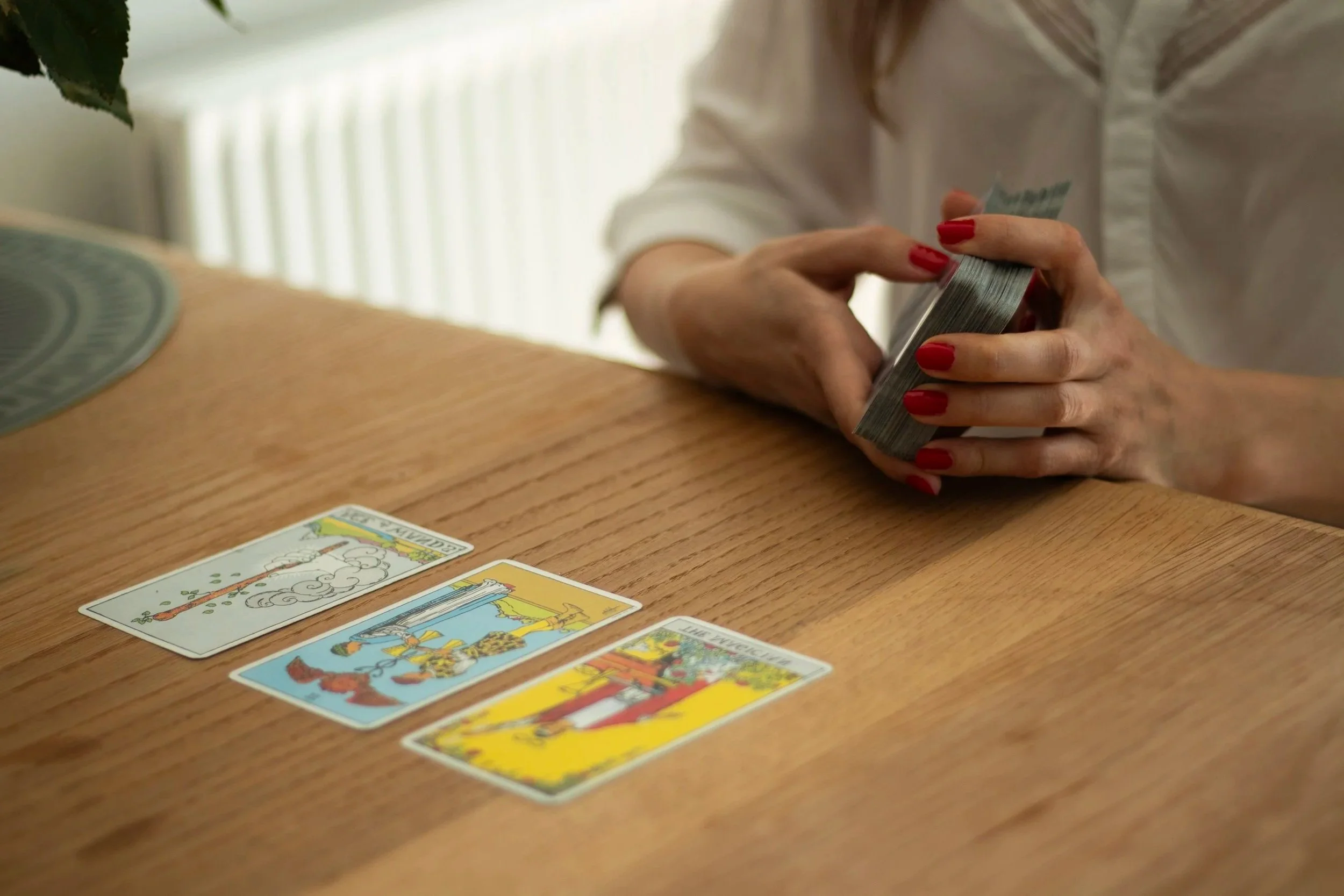 Hands holding a deck of tarot cards, while a few cards are already on the table.