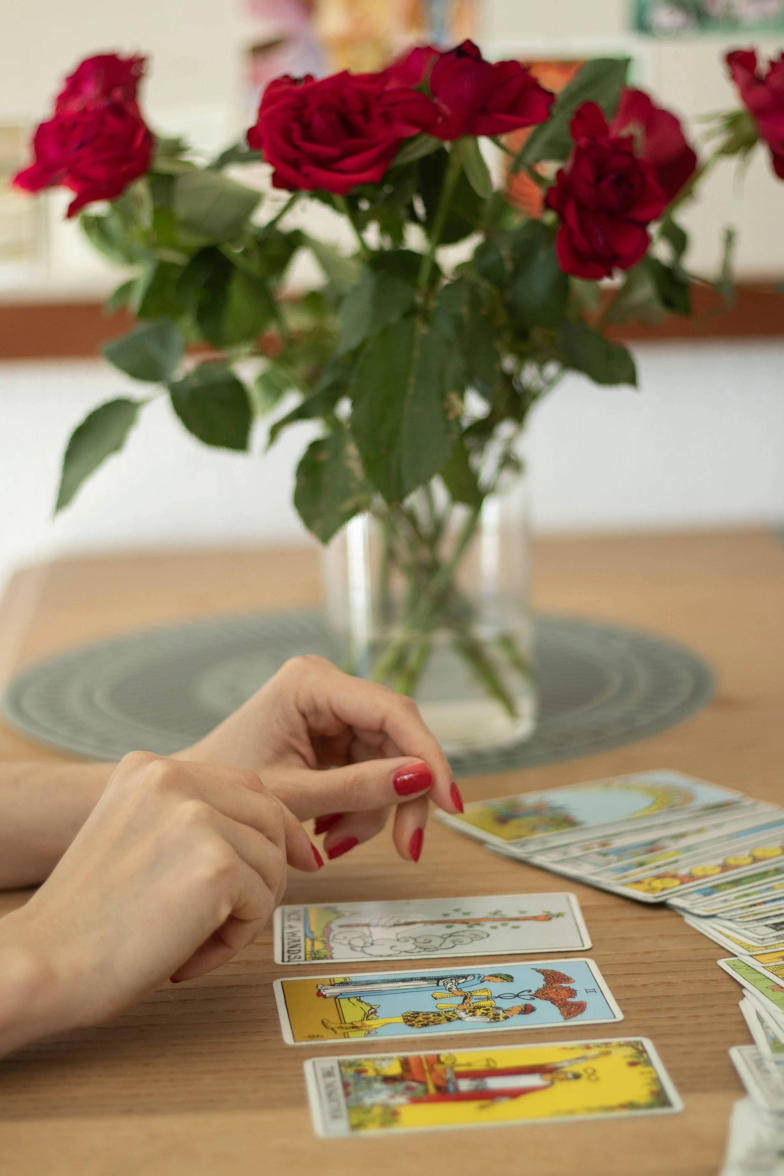Slanke  hænder der peger på tre tarotkort, som ligger på et bord.