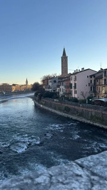 Scenic view of a river with buildings along the bank and a tall church steeple against a clear blue sky.