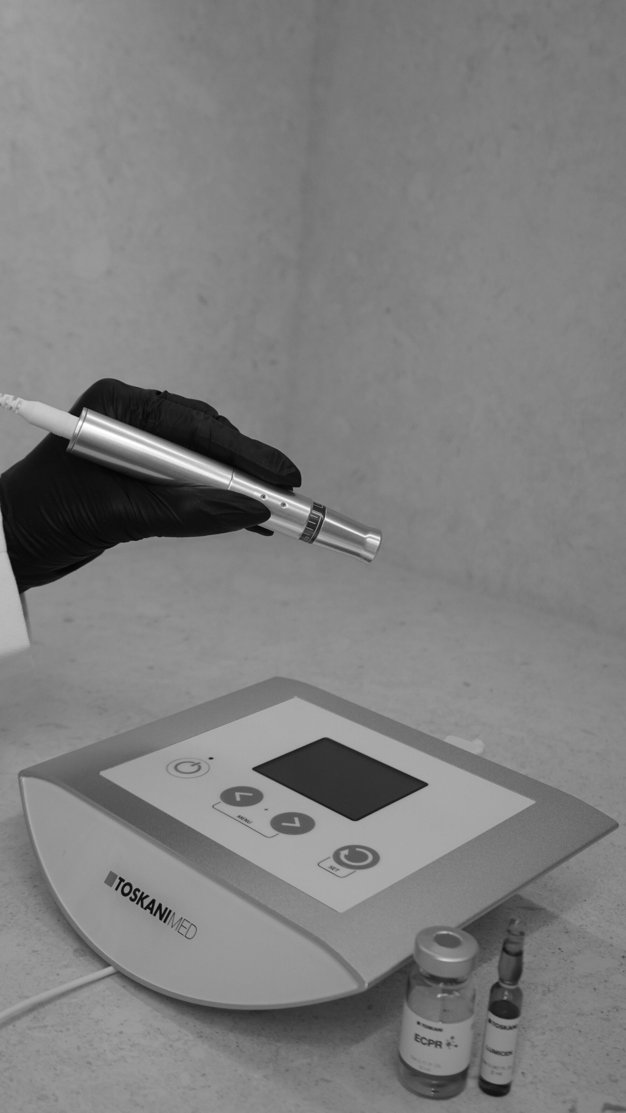 A hand wearing a black glove holding a pen-like device over a medical machine, with small vials labeled 'ECPR' beside the machine.