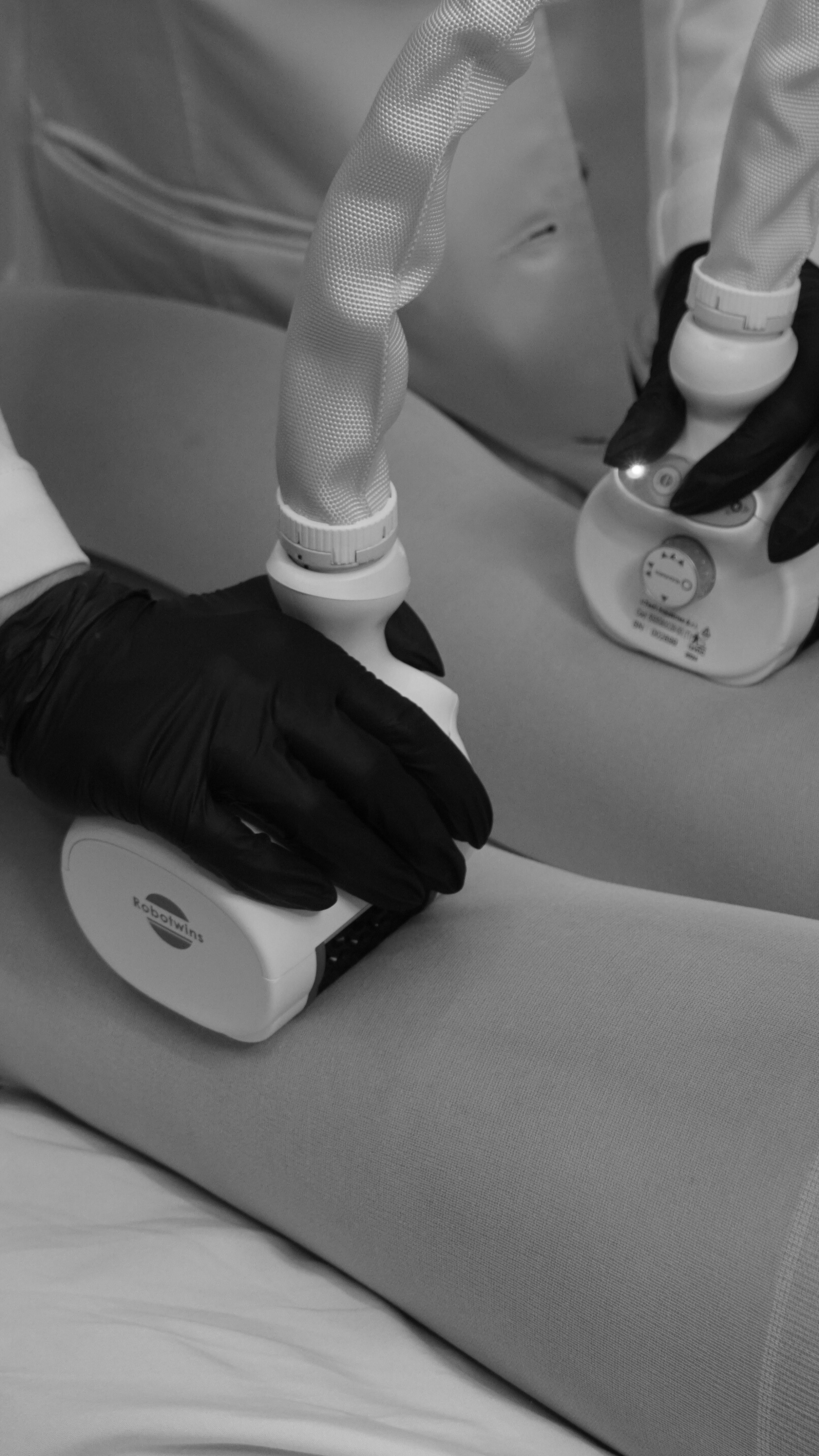 Medical professionals using a robotic device to perform a procedure on a patient, wearing black gloves.