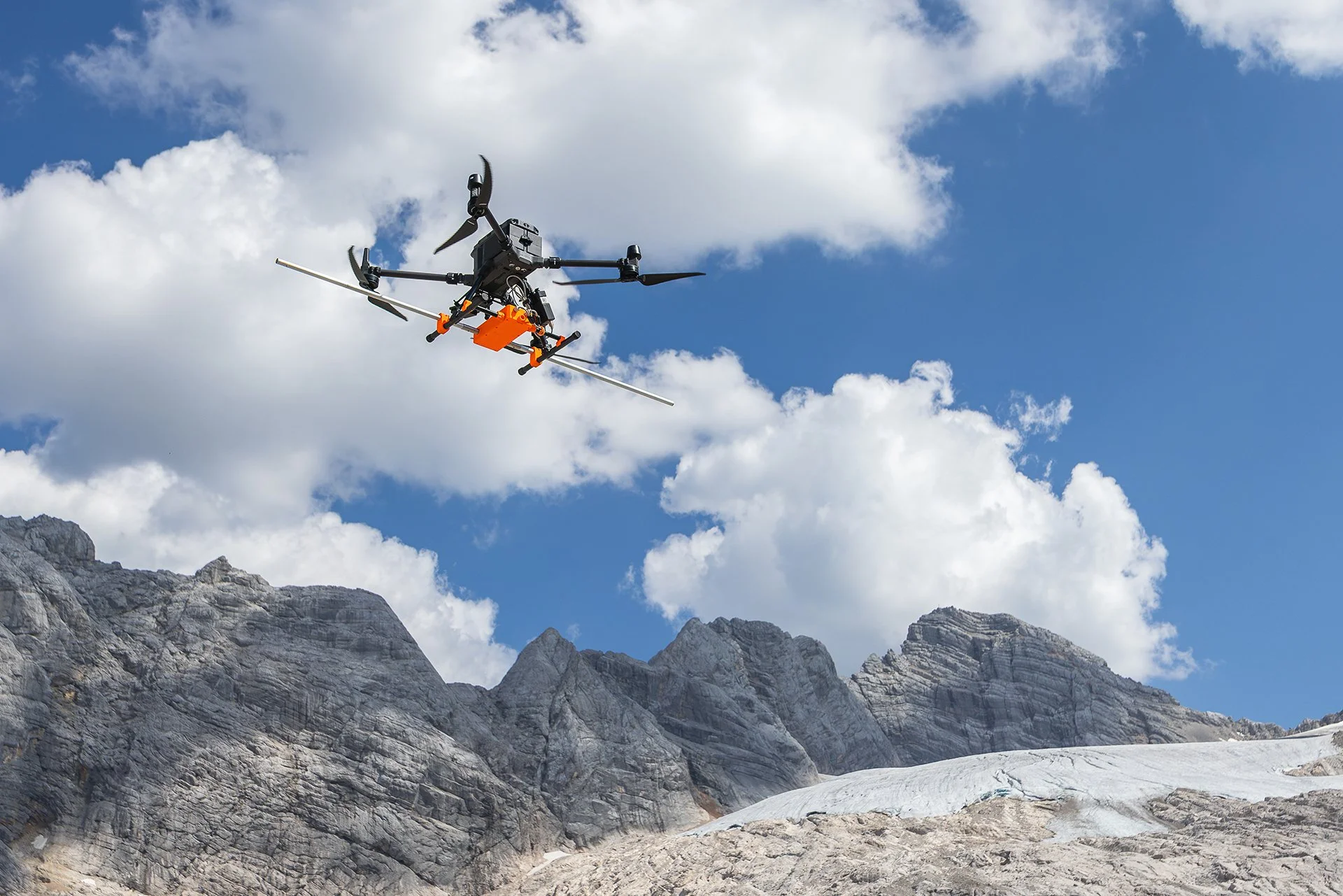 A drone flying above a rocky mountainous landscape with clouds and blue sky in the background.