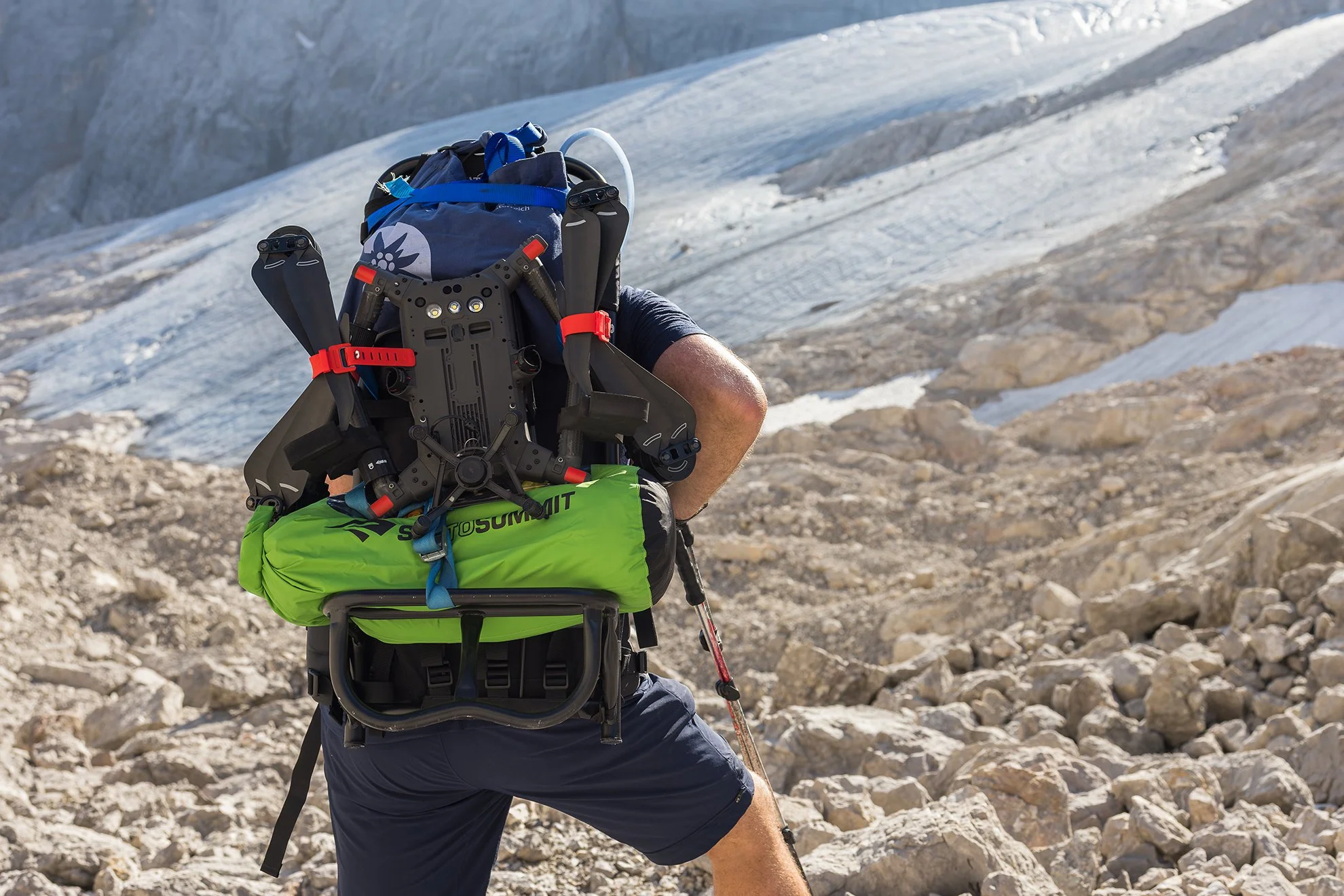 A person with a backpack and hiking gear climbing on rocky terrain near snow-capped mountains.