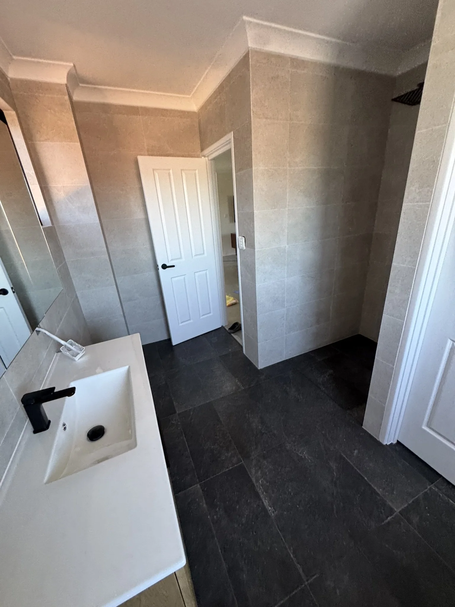 Bathroom with a white countertop sink, black faucet, mirror, and a door leading to a shower area with beige tiled walls and a black showerhead.