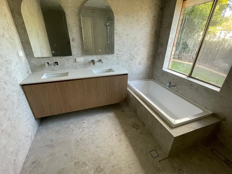 Bathroom with a double sink vanity, a large bathtub next to a window, and a frameless glass shower inside a mirrored cabinet.