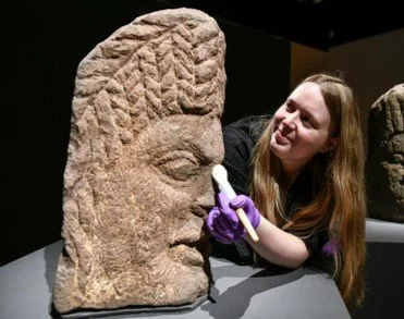 Tullie Curator Elsa gives one of the Carlisle Heads a professional clean before the "Digging Deeper" Exhibition in 2023. 
Stuart Walker Photograph.