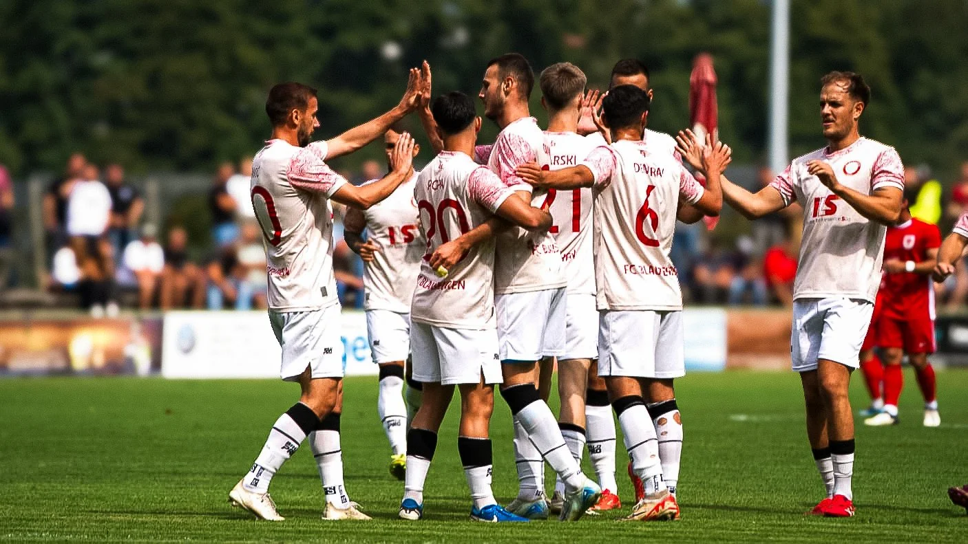 Fußballspieler in weißen Trikots feiern auf dem Spielfeld.