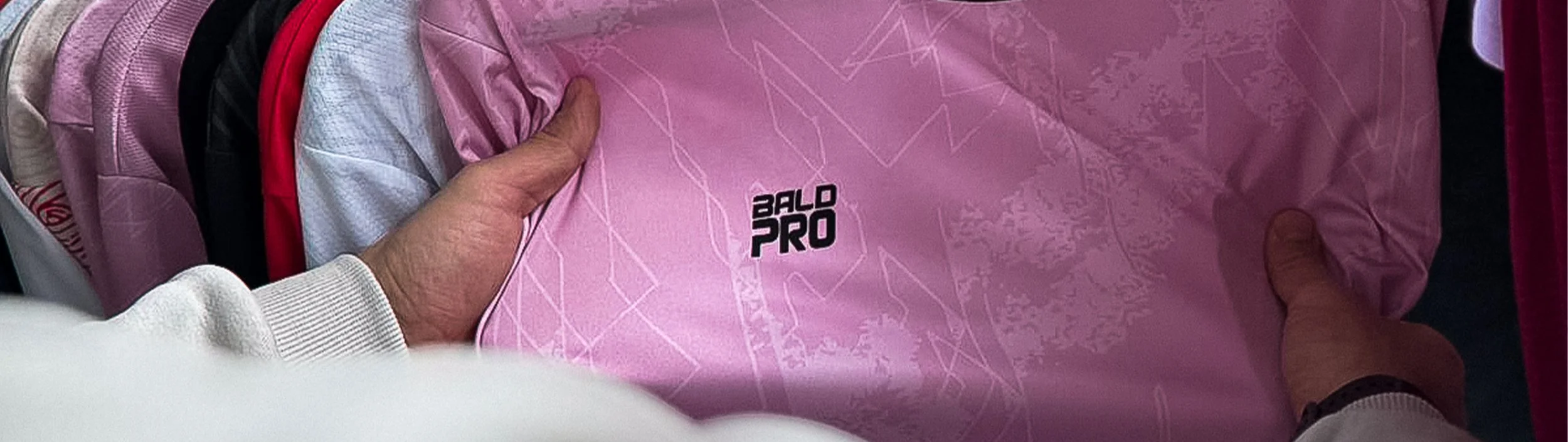 Hände halten eine pinke Trikot mit dem Schriftzug 'BALD PRO'.